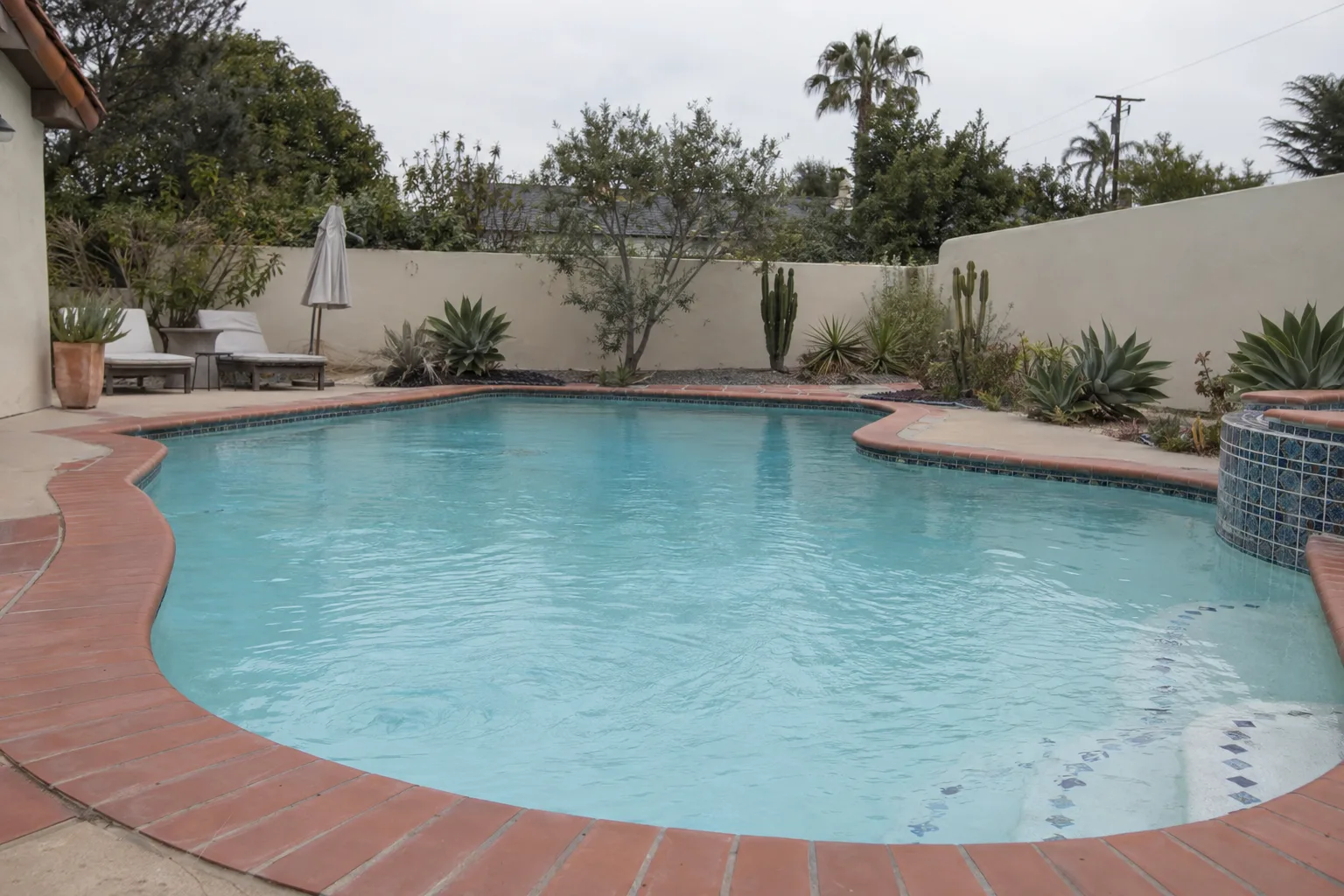 A clear blue residential swimming pool with white PVC coping and drought-tolerant landscaping under a bright Torrance sky